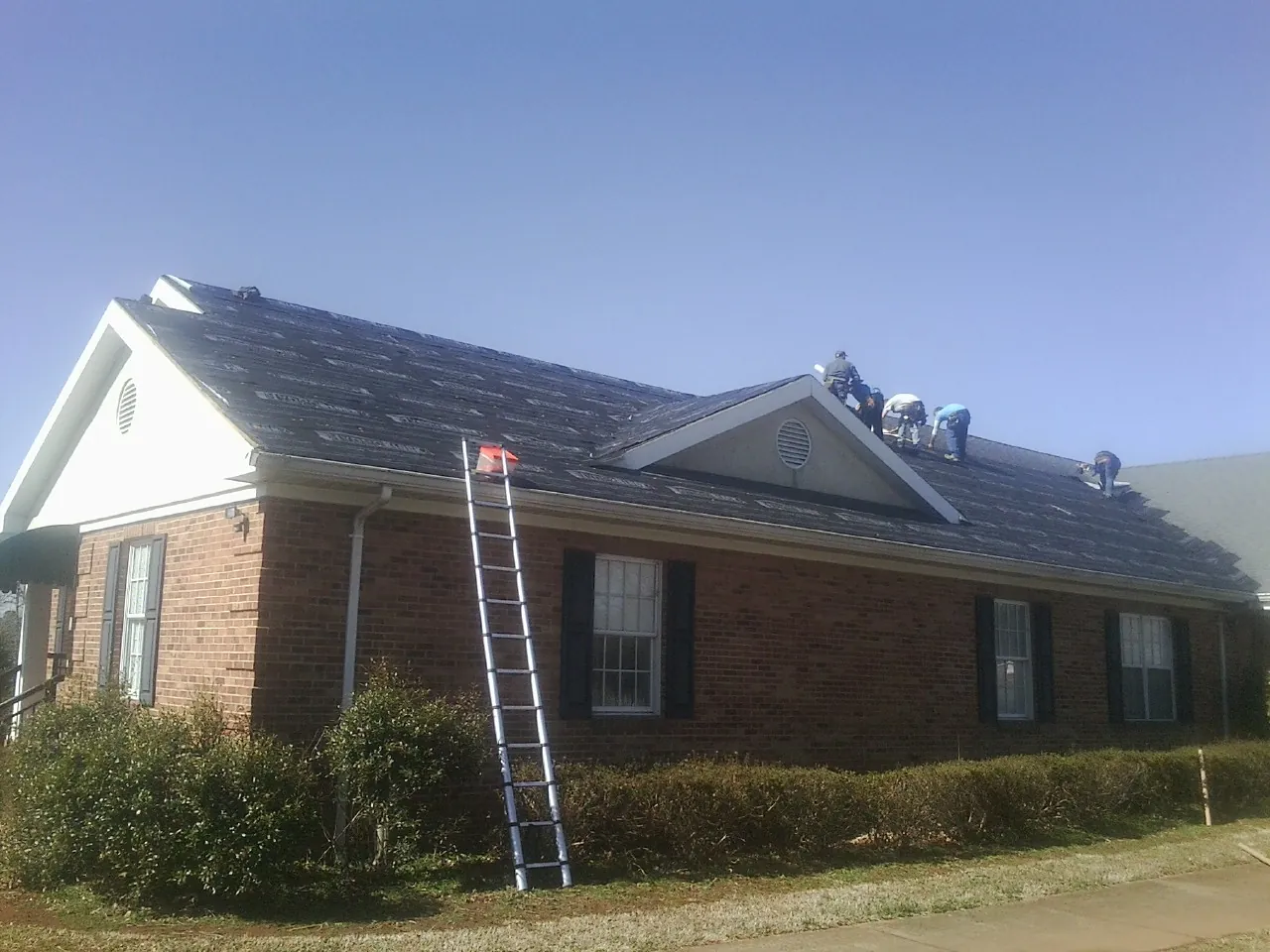 Crew tearing shingles off a brick ranch roof with a ladder set — Metal Roof Repair work by our crew in Lonedell