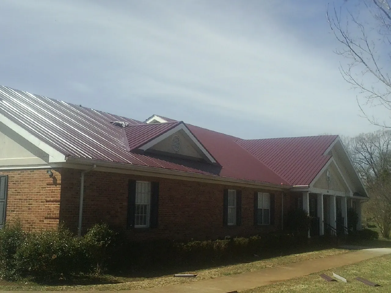 Red metal roof with gabled entries on a long brick building, from a Hail Damage Roof Repair job in Lonedell