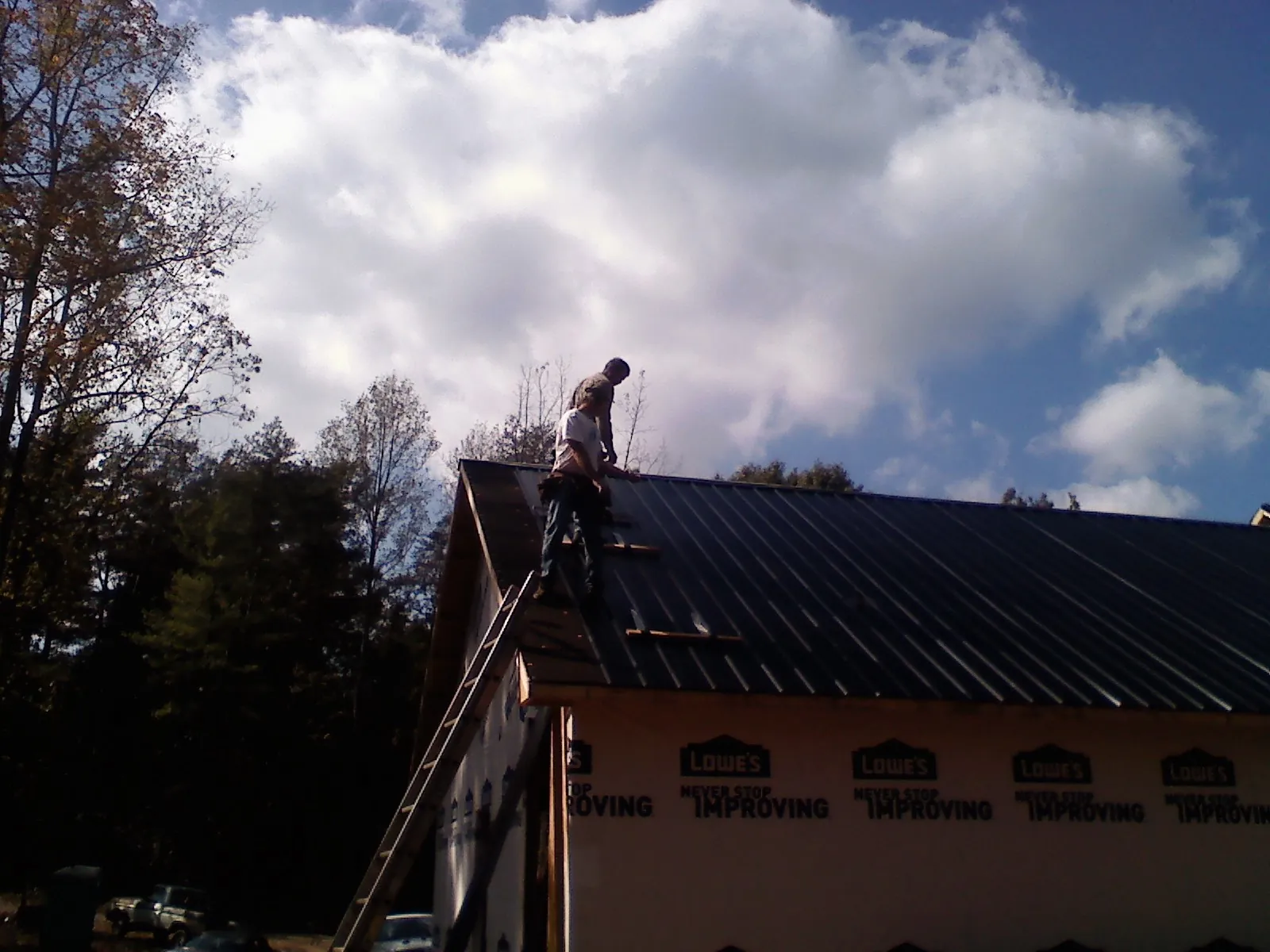 Roofer fastening dark metal panels high against a cloudy sky, from a Roof Inspection job in Lonedell