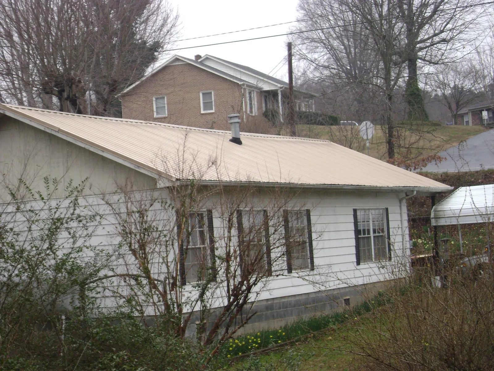 Tan metal roof on a white sided house set into a hillside — Commercial Roofing by Roofing Brothers in Lonedell