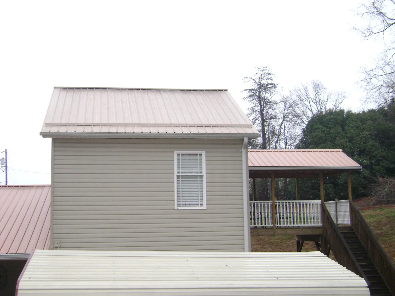 Tan metal roofs on a two story addition and attached porch, from a Roof Replacement job in Lonedell